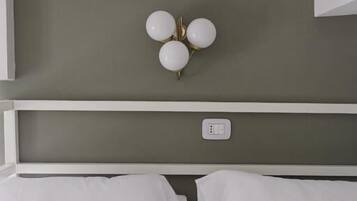 Un lit avec du linge de lit blanc, une tête de lit blanche et un luminaire fixé au mur, doté de trois ampoules sphériques.