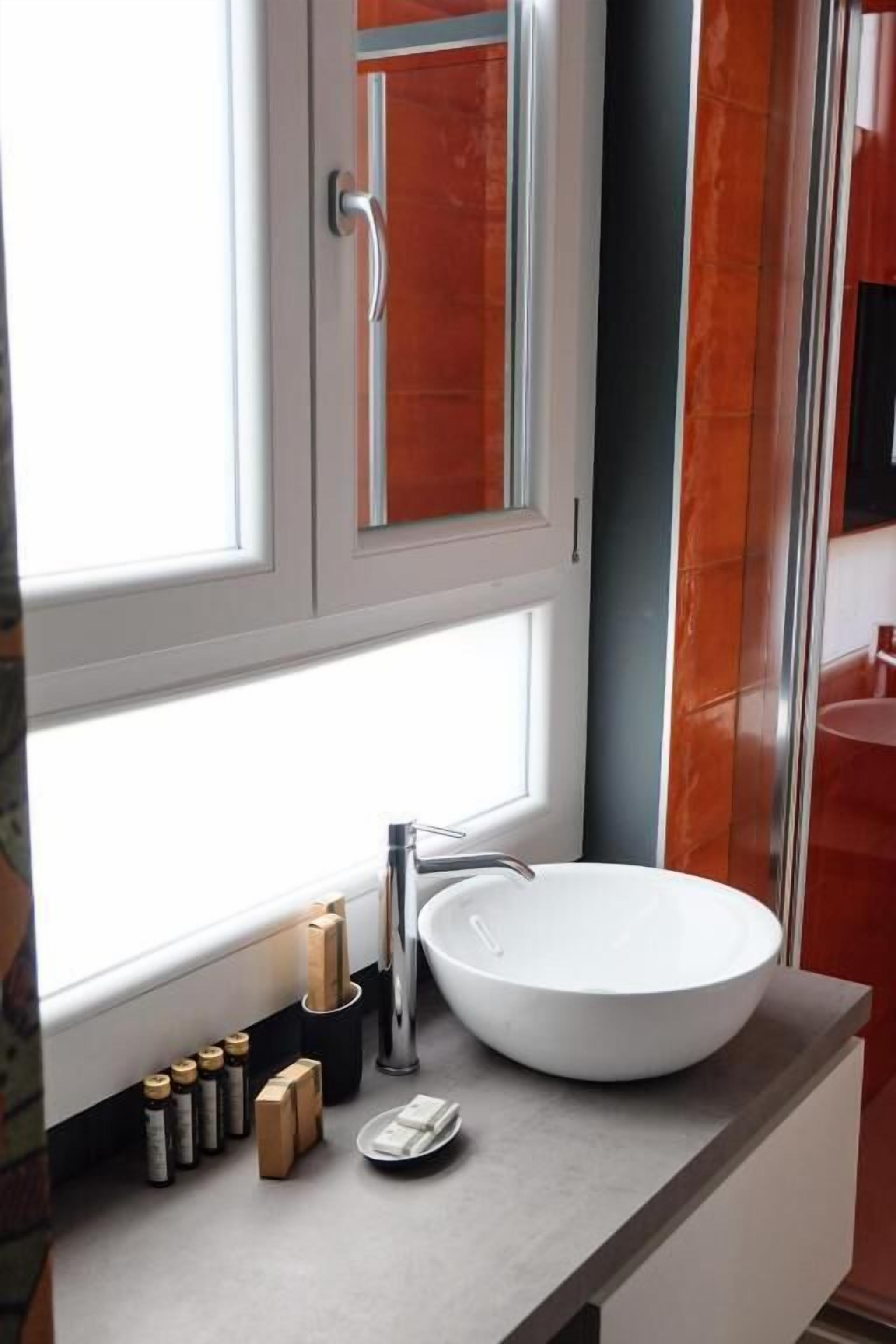 Un bagno con un lavandino bianco, uno specchio e una finestra. Sul mobile ci sono articoli da toilette.