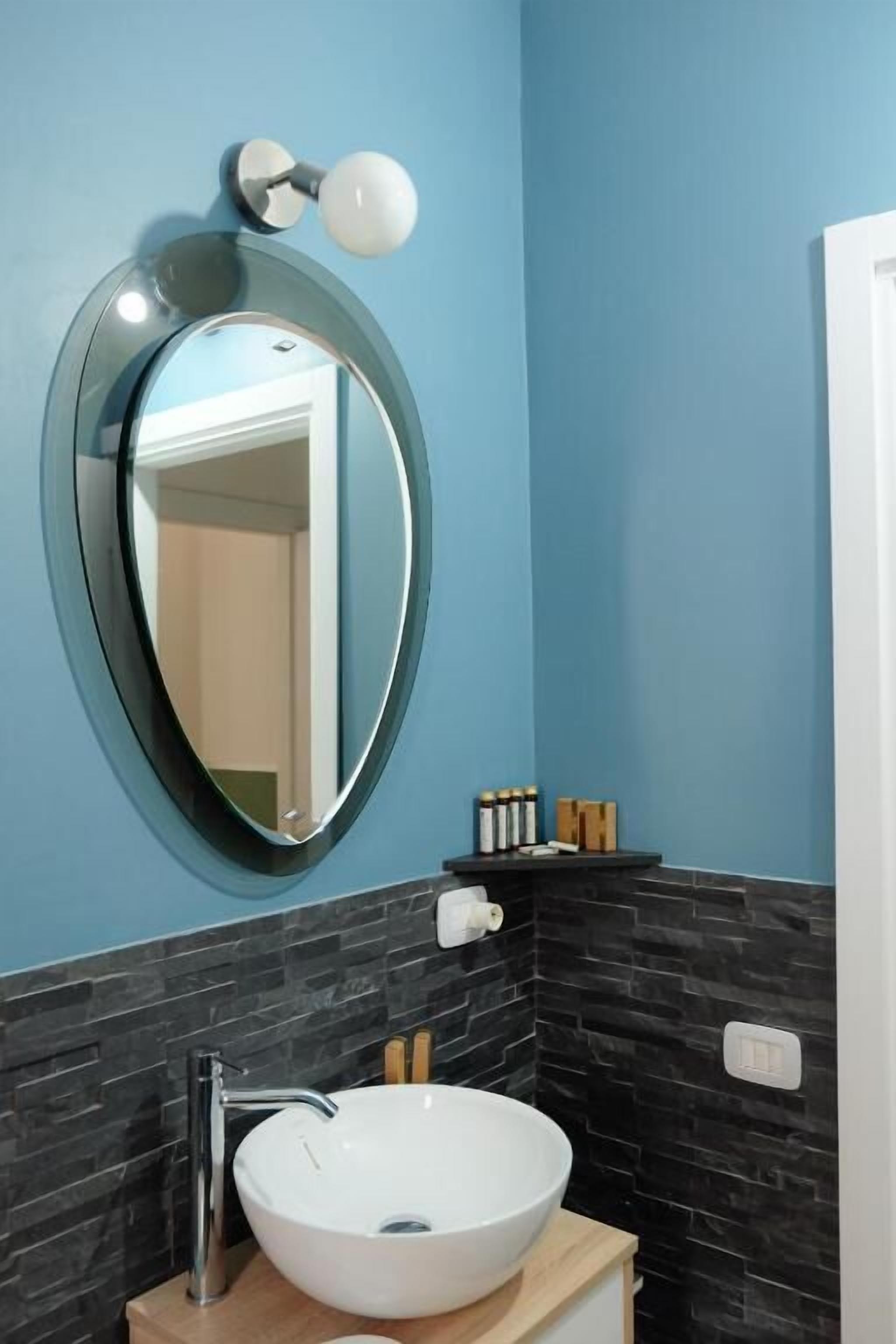 A bathroom with a round mirror, white sink, and black tiled walls.