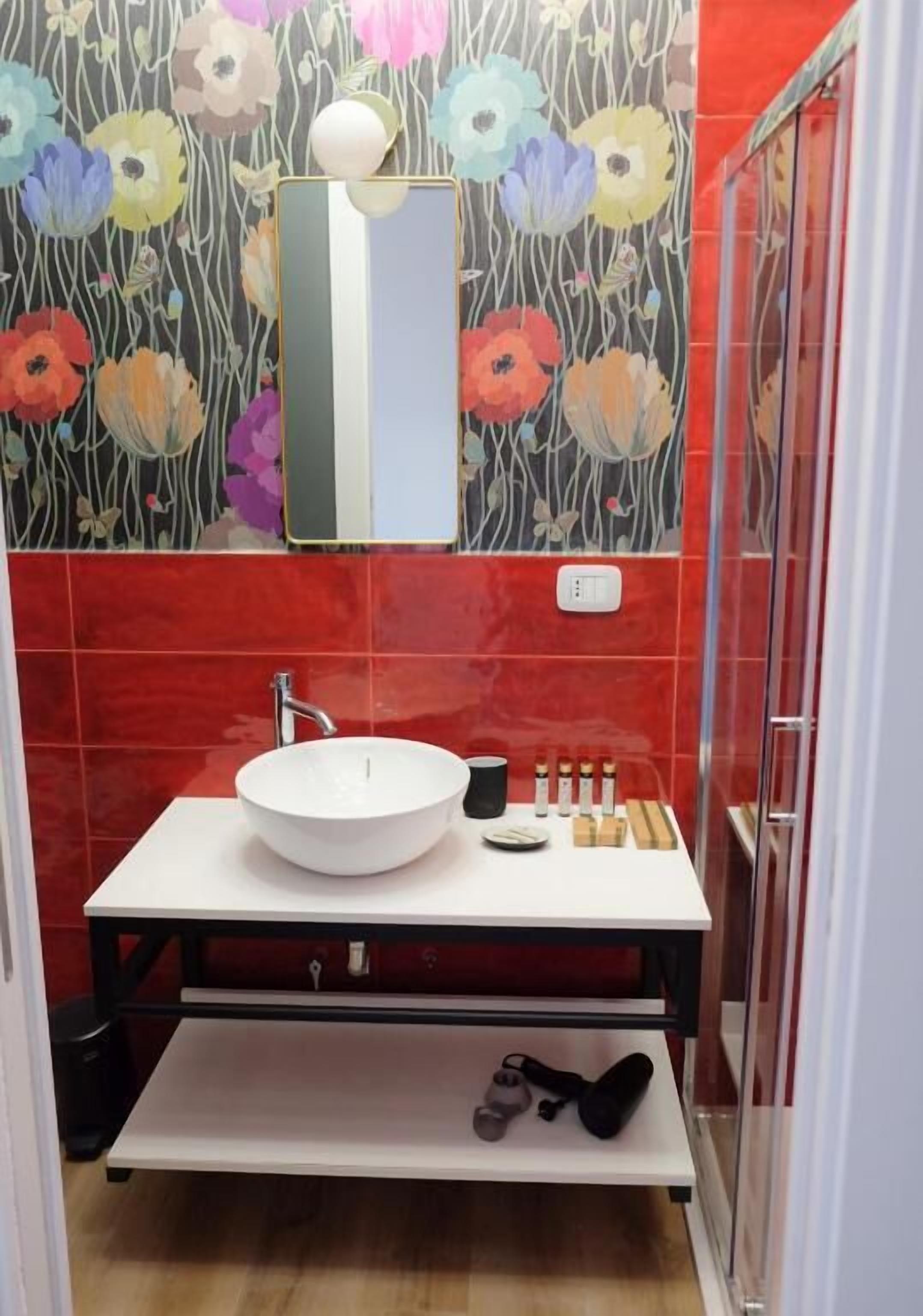 Un baño con lavamanos blanco, espejo y repisa con artículos de aseo.