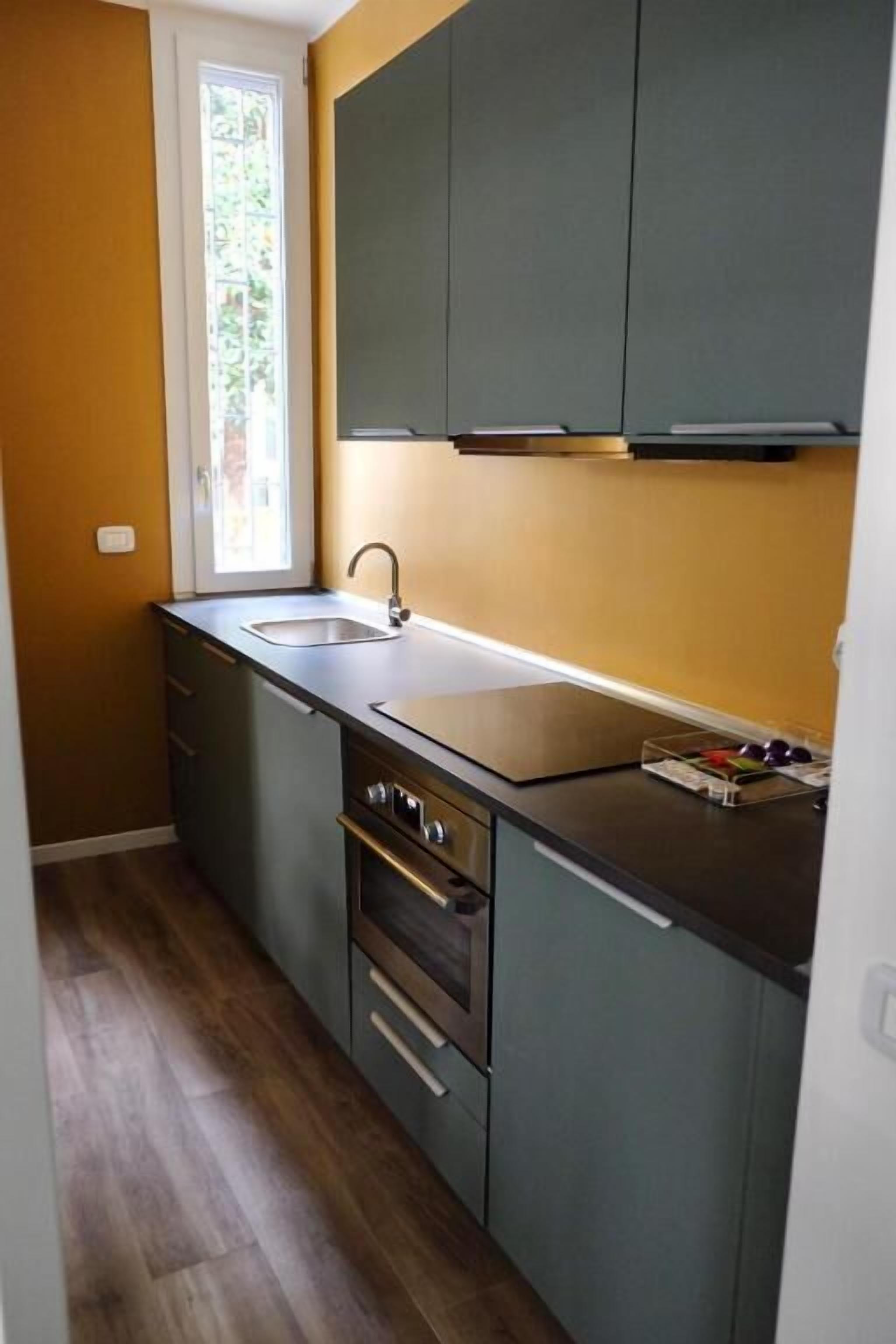 A compact kitchen with a single sink, a stove, and a window with a view of greenery.