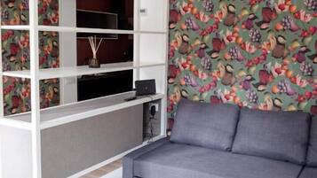 Ein modernes Wohnzimmer mit einer grauen Eckcouch, einer weißen Regaleinheit und ornamentalem Wandpapier.