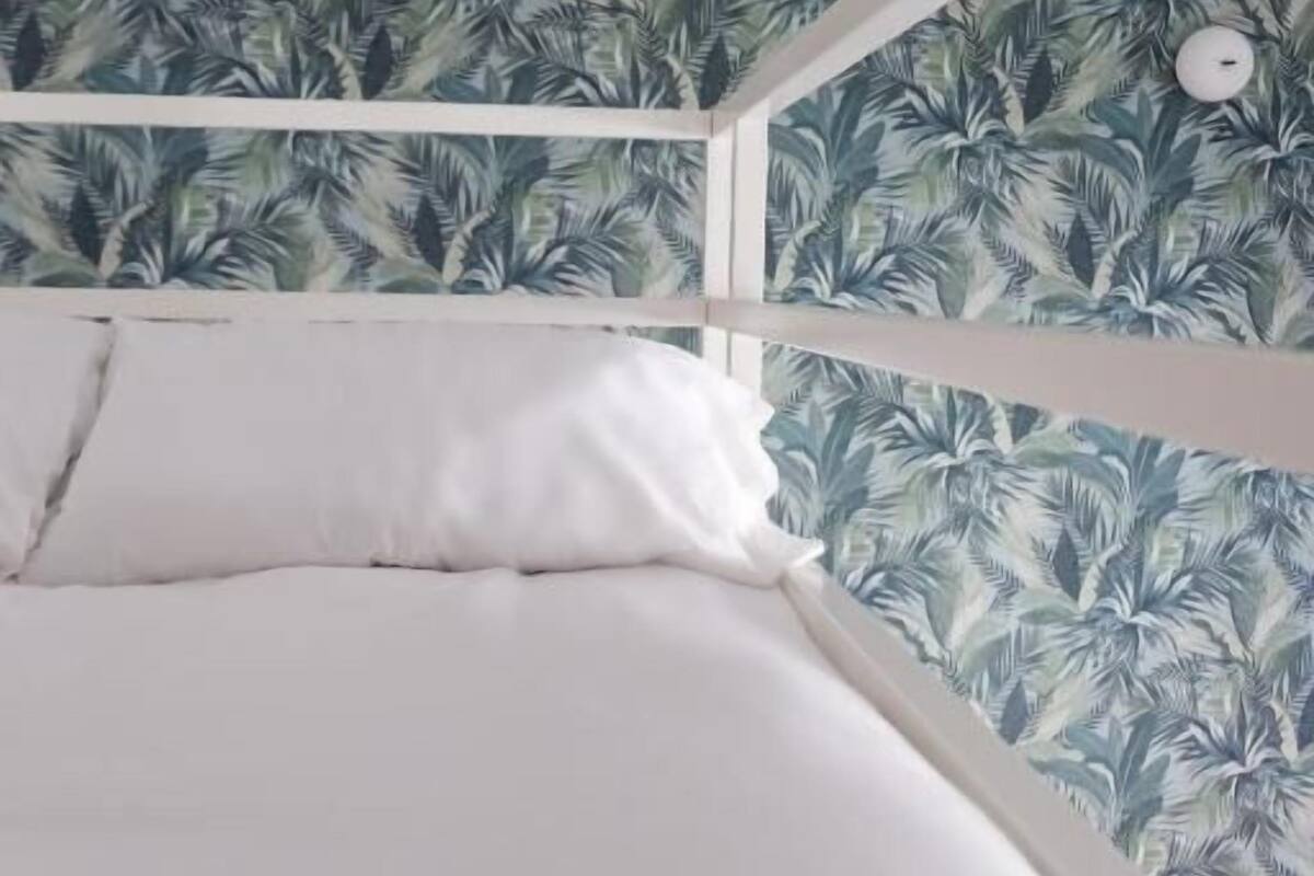 A bunk bed with a white frame and a tropical leaf-patterned wall.