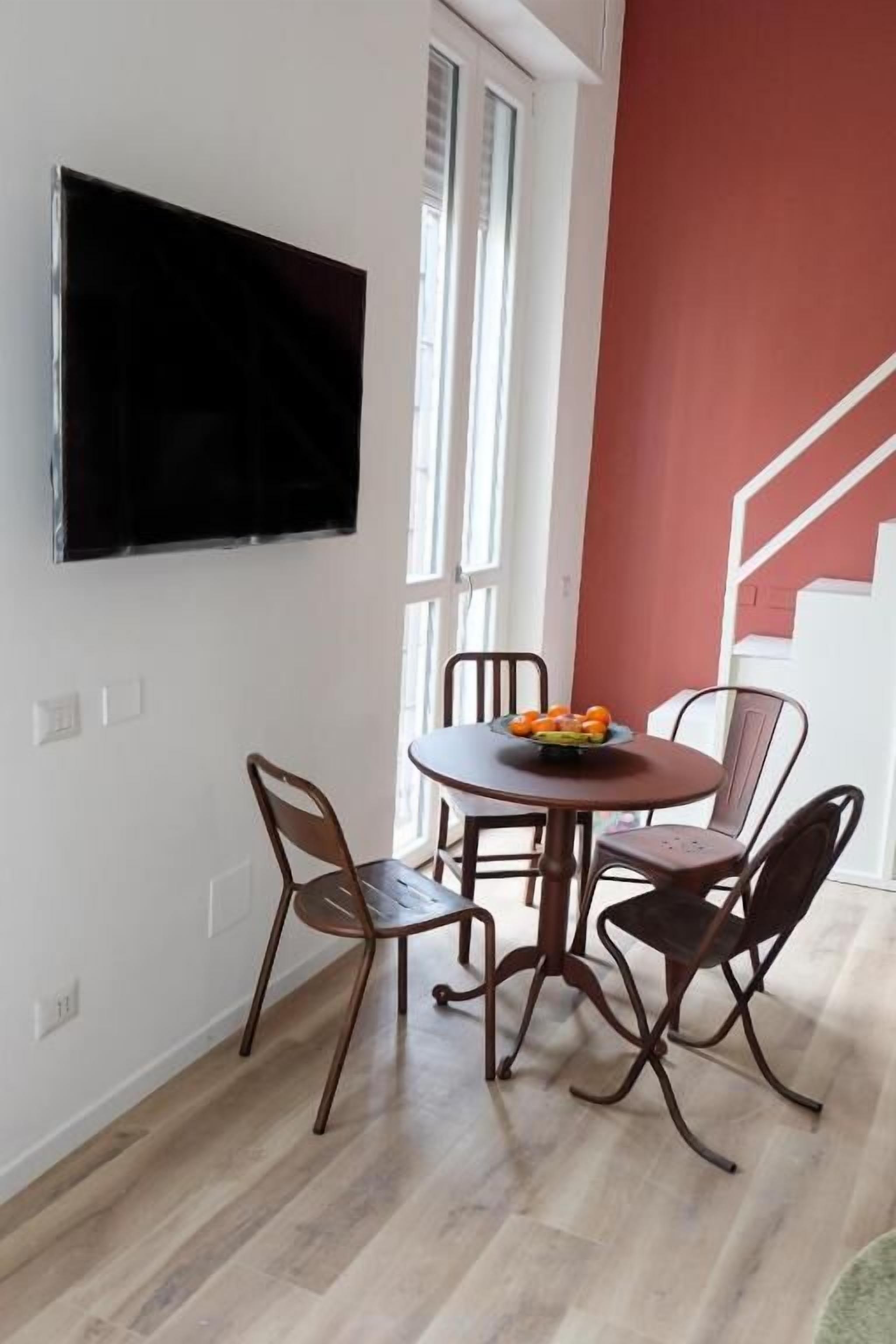 A dining area with a round table, four chairs, and a flat-screen TV mounted on the wall.