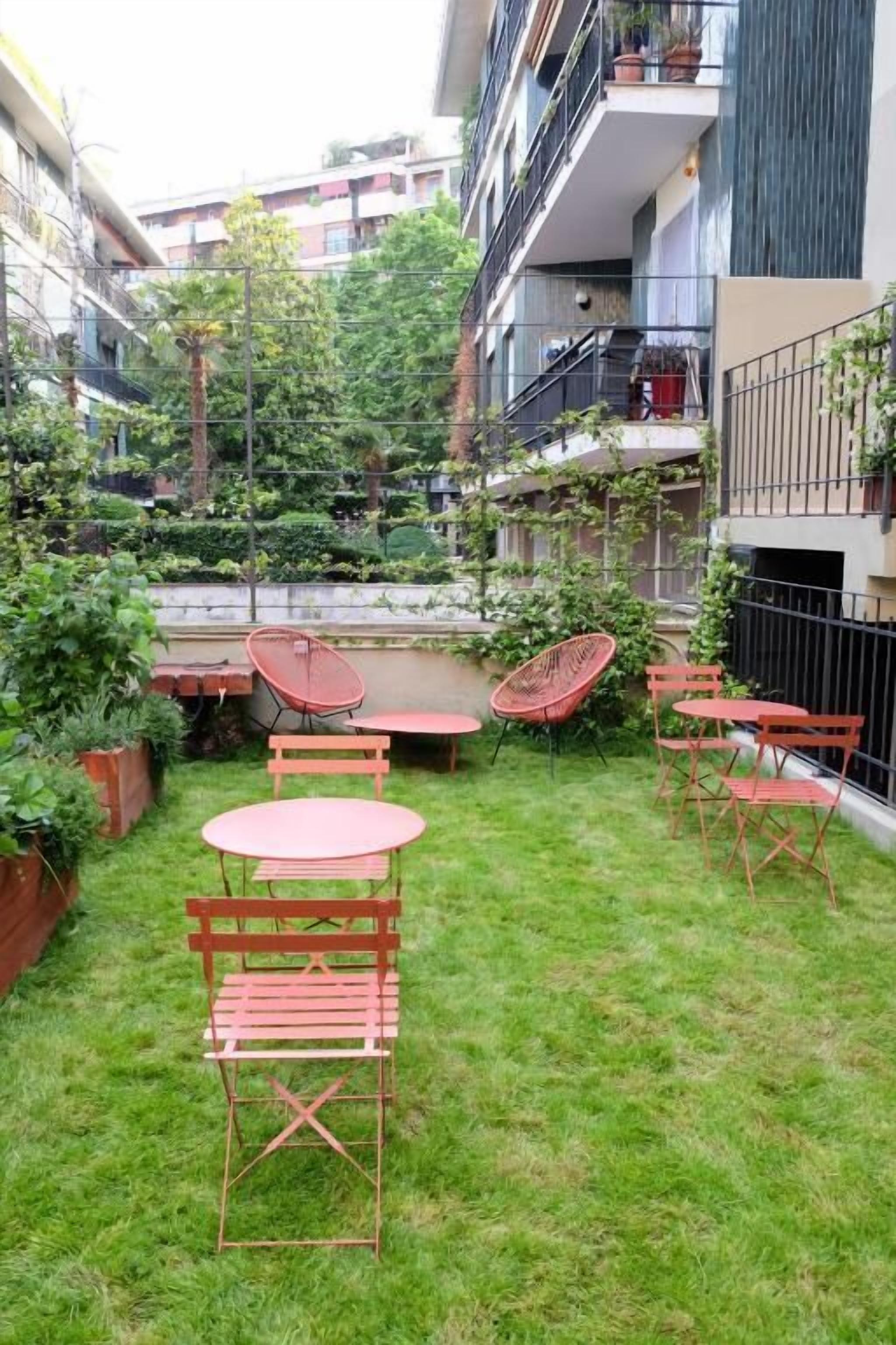 A courtyard with a small lawn, a wooden table, and several chairs.