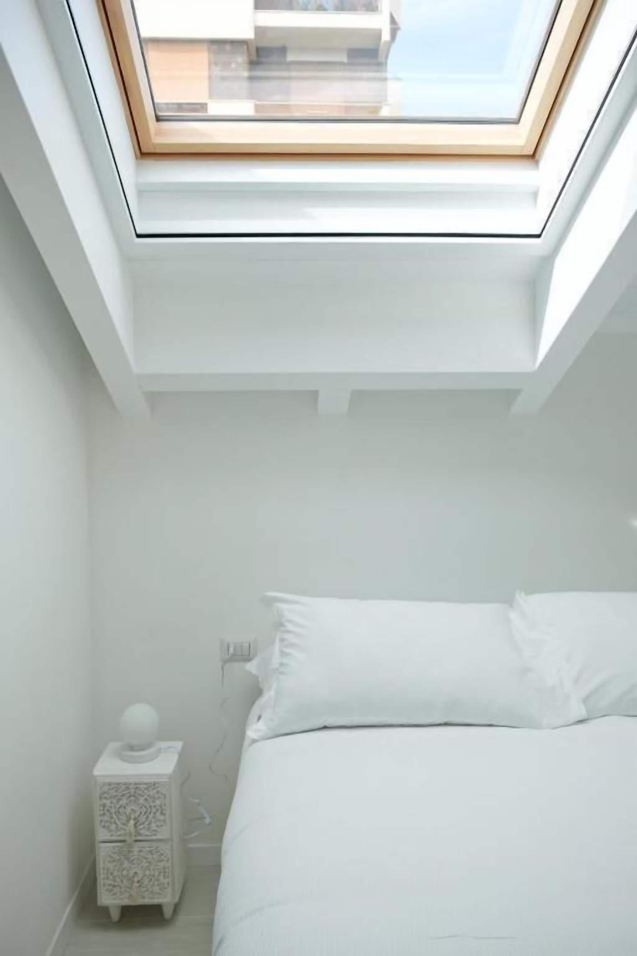 A bedroom with a skylight, a bed, a nightstand, and a wall socket.