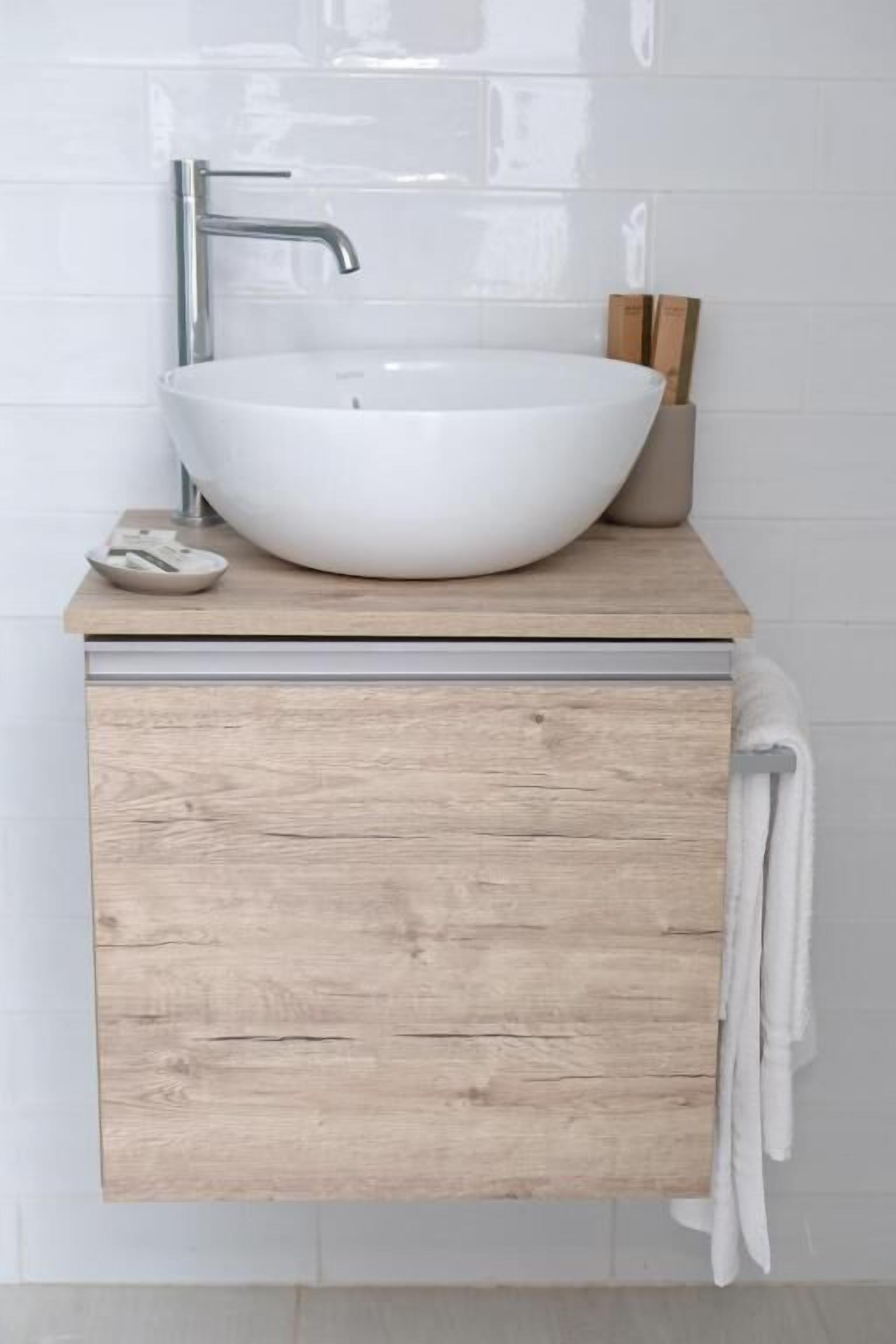 A bathroom with a white vessel sink, wooden vanity, and a towel hanging on the wall.