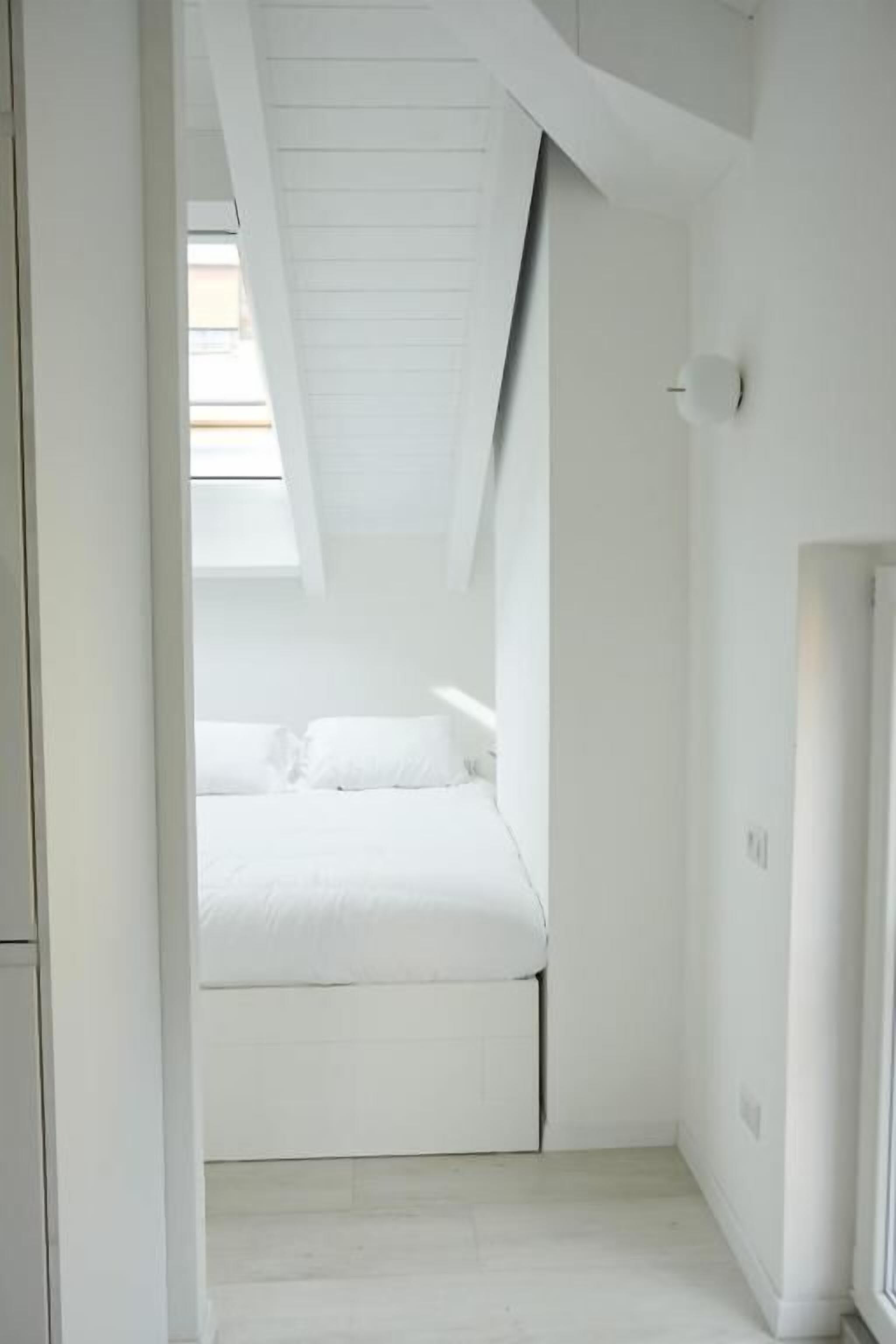 Une pièce minimaliste avec un plafond en pente, un lit et une fenêtre.