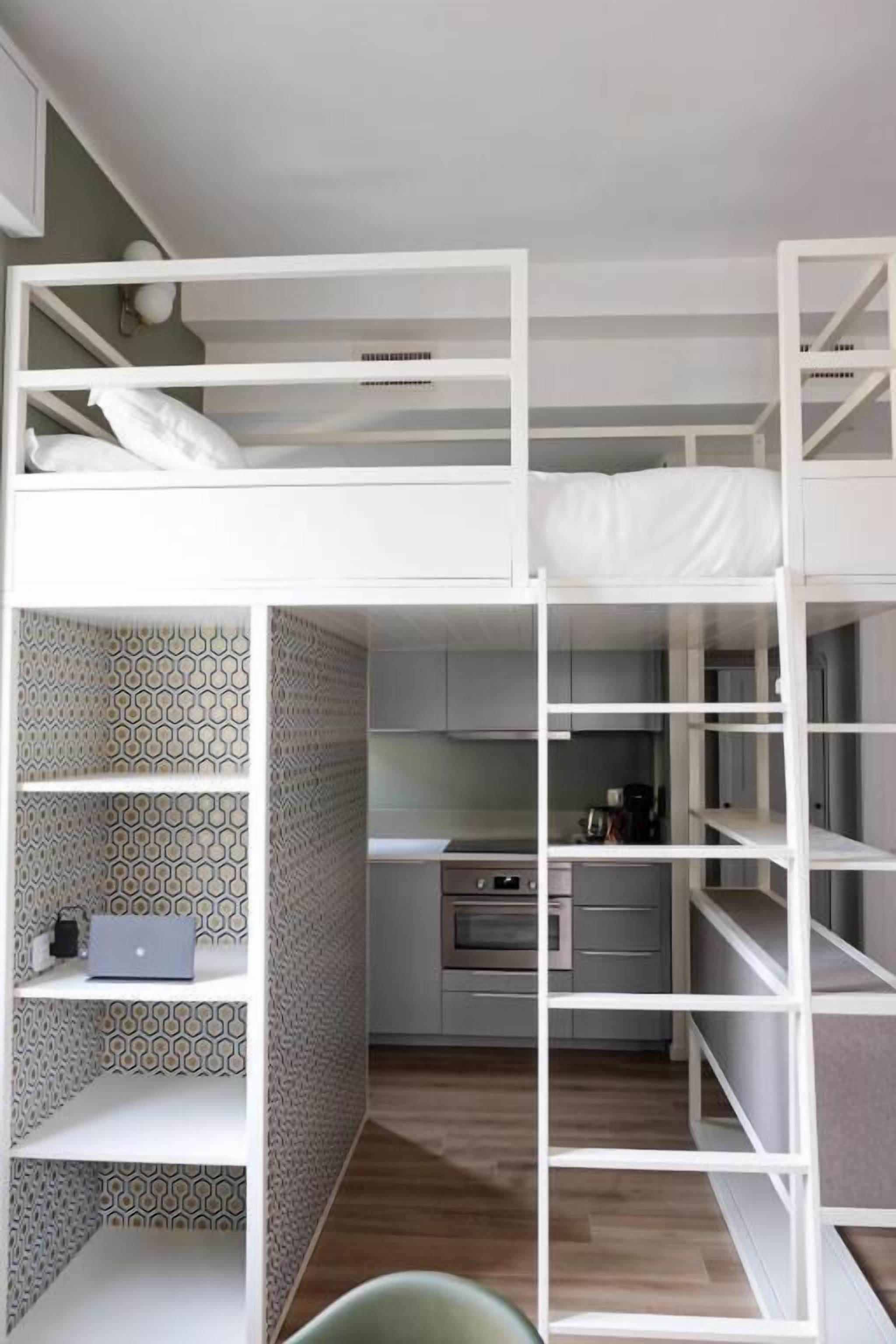 Una cama litera con un ordenador portátil en la parte inferior, una zona de cocina con microondas y una pared con un diseño estampado.
