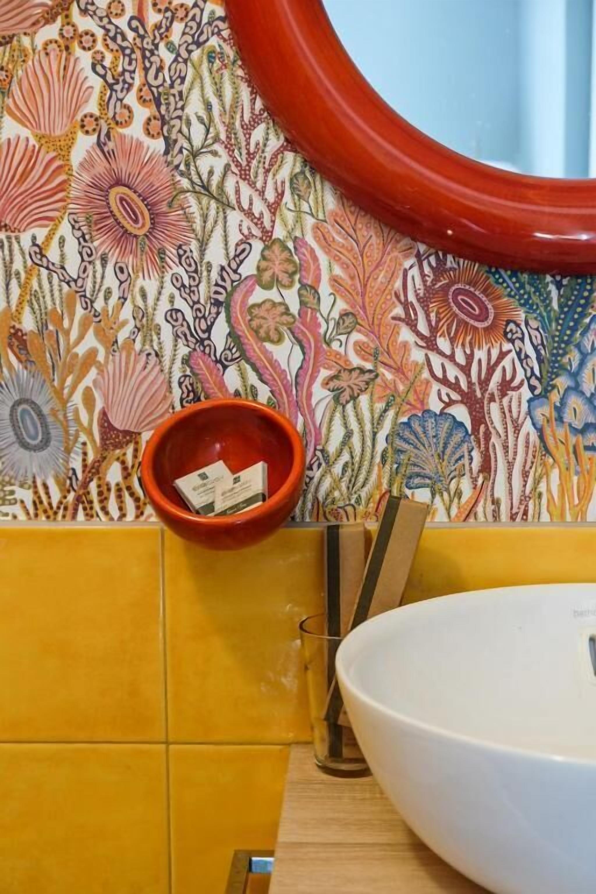 A bathroom with a floral wallpaper, a red bowl, and a white sink.