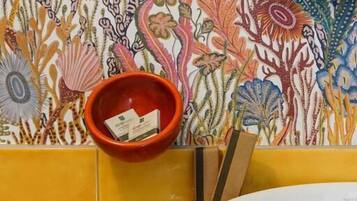 A bathroom with a floral wallpaper, a red bowl, and a white sink.