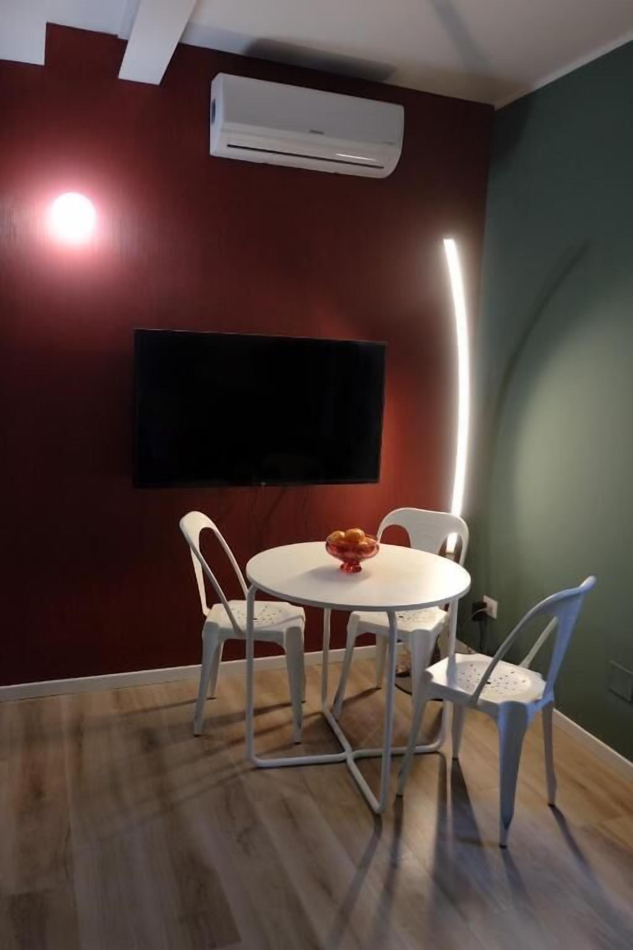 Een kamer met een ronde tafel, vier stoelen, een flatscreen-televisie aan de muur en een airconditioner.