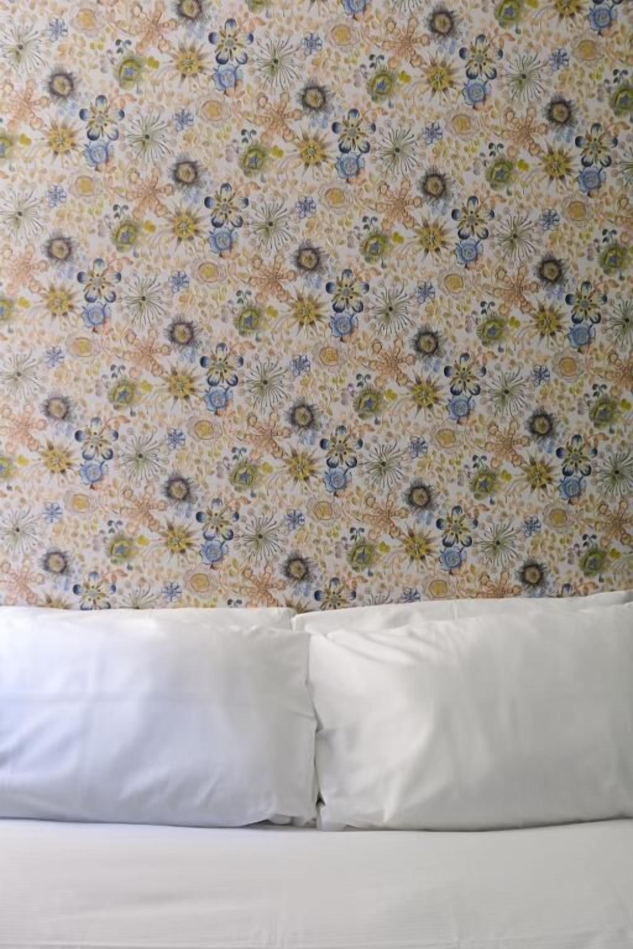 A bed with white bedding and a floral-patterned wall behind it.