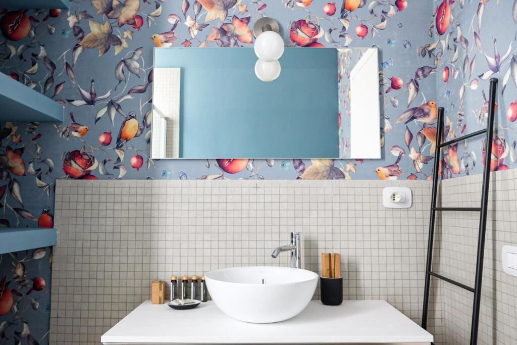 Une salle de bain avec un lavabo blanc, un miroir et un papier peint à motifs floraux.