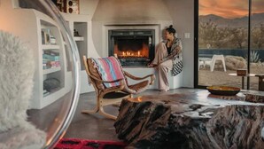 A cozy living room with a fireplace, a large window with a view of the desert, and a comfortable seating area.