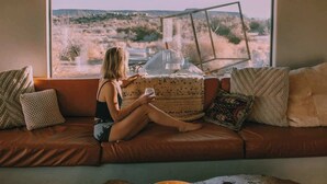 A person sitting on a leather sofa by a large window overlooking a desert landscape.
