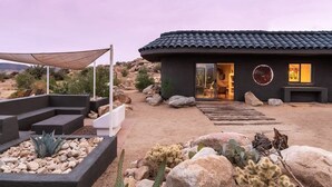 A modern house with a dark exterior, a tiled roof, and a well-maintained garden with rocks and cacti.