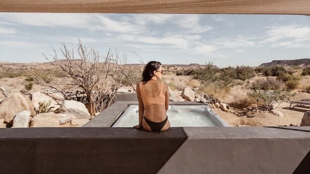 A person sitting in a hot tub outdoors with a desert landscape in the background.