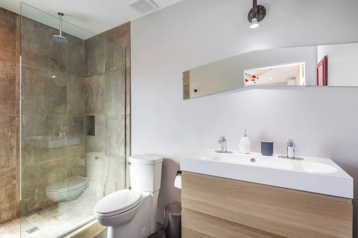 A modern bathroom with a glass-enclosed shower, a white toilet, and a wooden vanity with a white sink.
