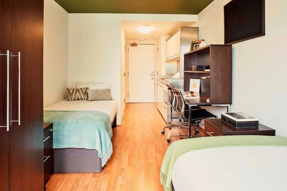 A compact room with two beds, a desk with a chair, and a wardrobe.