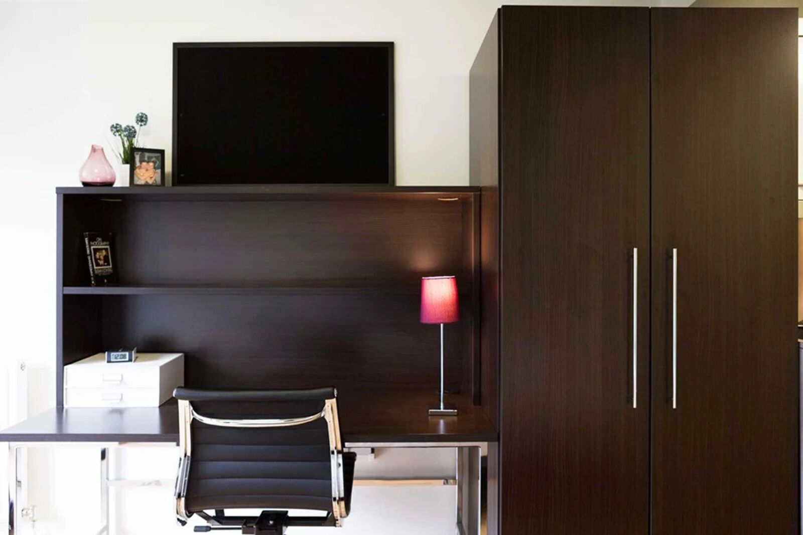 Un espace de bureau moderne comprenant un bureau, une chaise et un grand meuble en bois foncé.