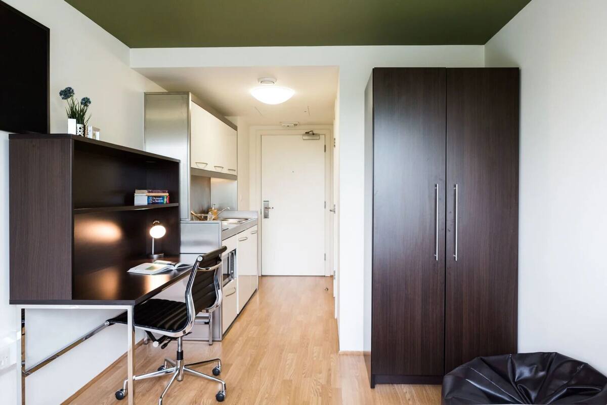 A compact kitchen with a dining area, a dark wooden wardrobe, and a small trash bin.