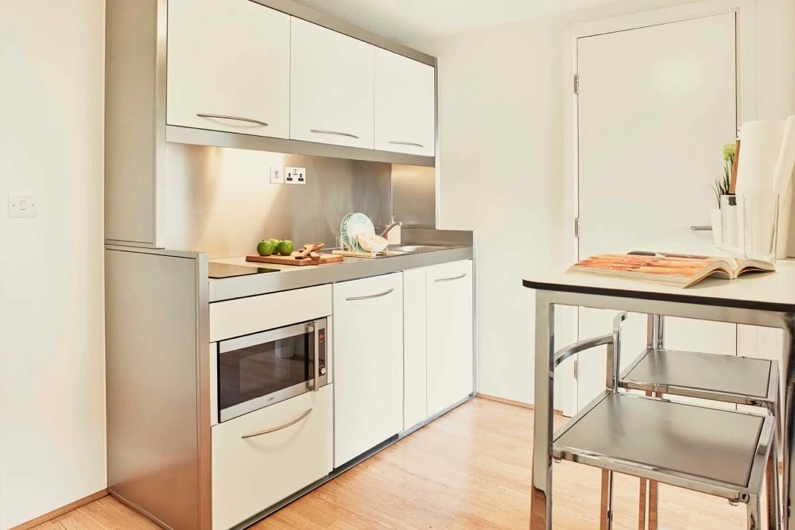 A modern kitchen with white cabinets, a built-in oven, and a small dining table.