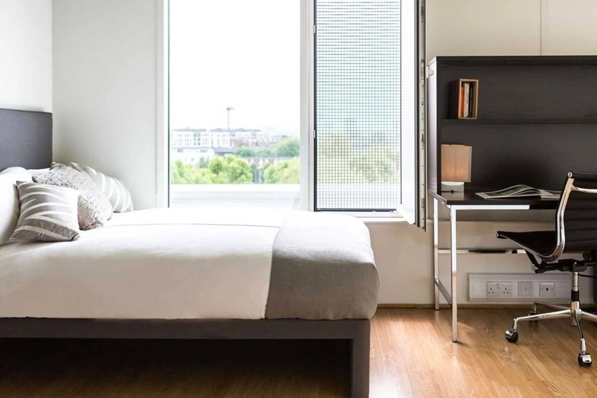 A modern bedroom with a bed, a desk, and a window with a city view.
