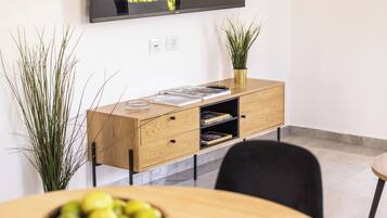 A modern living room with a wooden cabinet, a flat-screen TV mounted on the wall, and a potted plant.