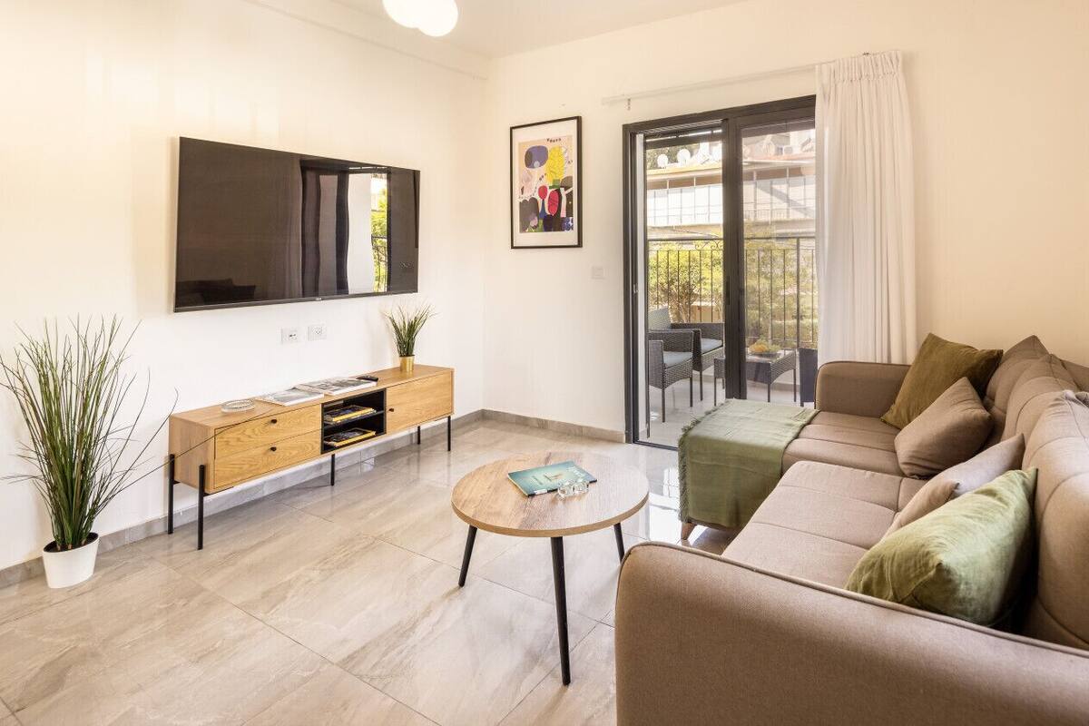 Un salon moderne comprenant un canapé, une table basse, un téléviseur fixé au mur, un petit meuble en bois et un balcon avec vue.