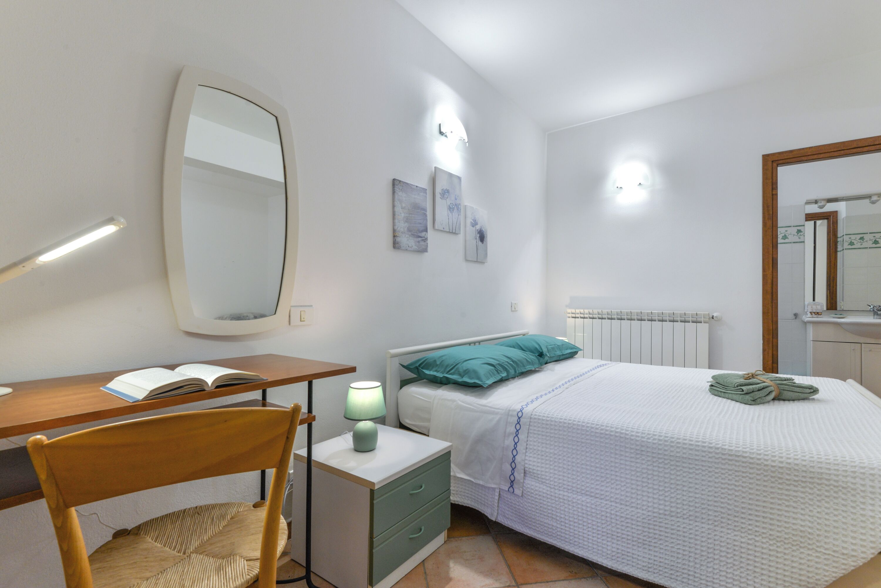 Un dormitorio con cama, mesita de noche, silla, escritorio y un espejo grande.