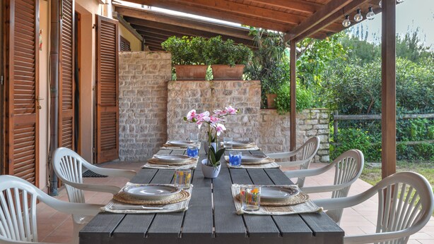An outdoor dining area with a stone wall, wooden shutters, and a covered roof.