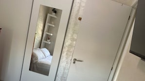 A bedroom with a bed, a wardrobe, and a mirror reflecting a bathroom with a sink and a towel rack. - Apartamento en Empuriabrava (Empuriabrava)
