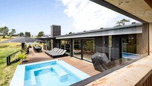 Uma área de piscina moderna ao ar livre, com hidromassagem, espreguiçadeiras e um deck de madeira.