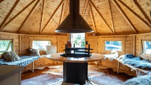 A log cabin interior with a central table, fur-covered benches, and a hanging light fixture. - Villa in Brabant With Spa and Sauna (Oirschot)