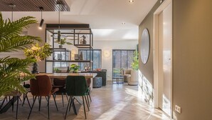 A modern kitchen with a dining area, wooden flooring, and a large window with blinds. - Villa in Brabant With Spa and Sauna (Oirschot)