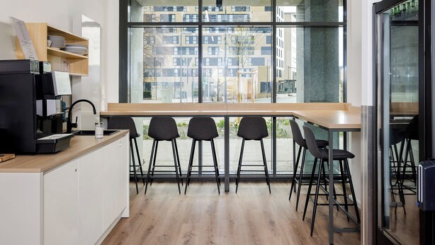 A modern kitchen with a large window, bar stools, and a coffee machine. - smartments Frankfurt Airport (Frankfurt)