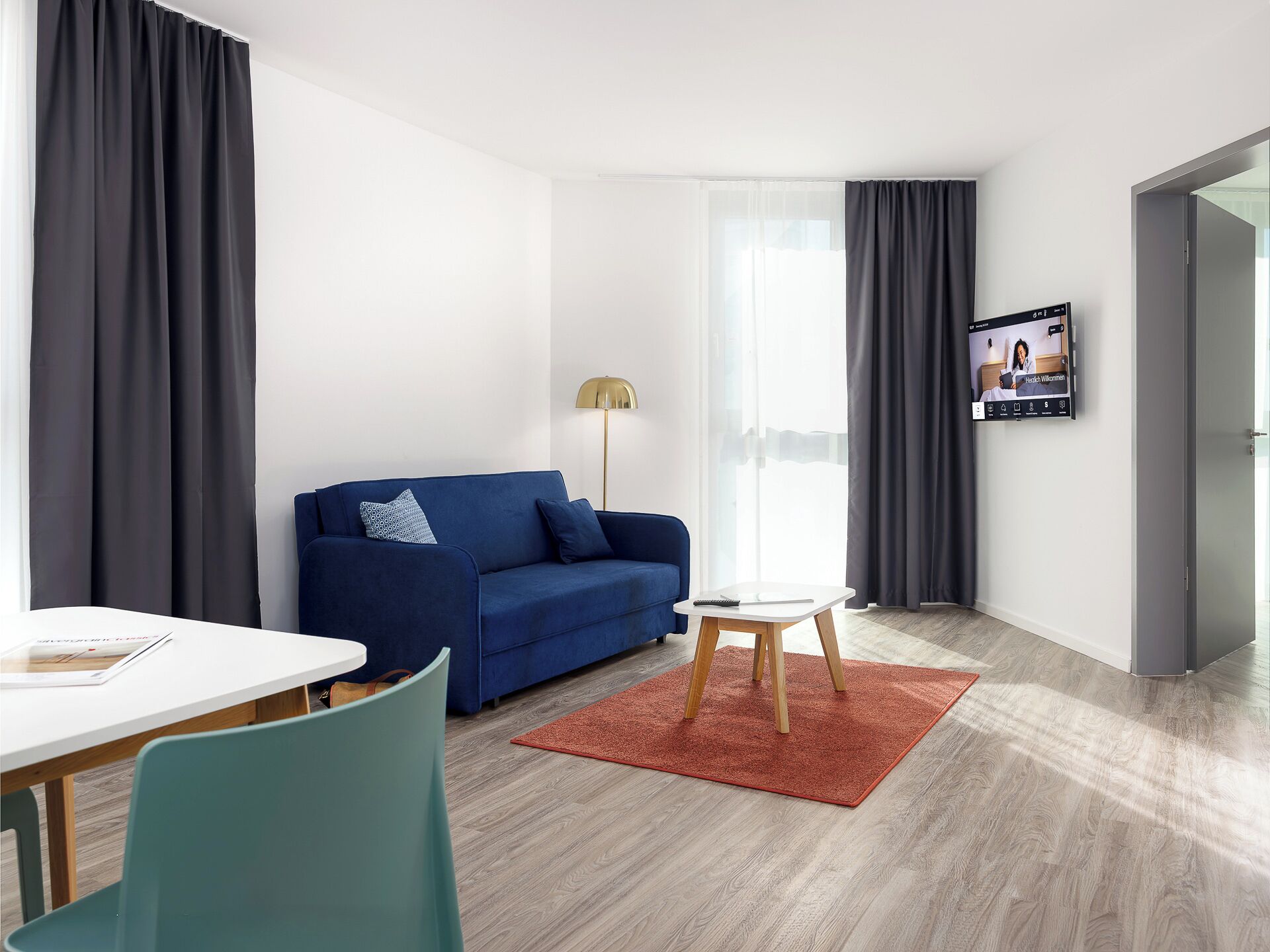 Een moderne woonkamer met een blauwe bank, een witte salontafel en een rood vloerkleed.