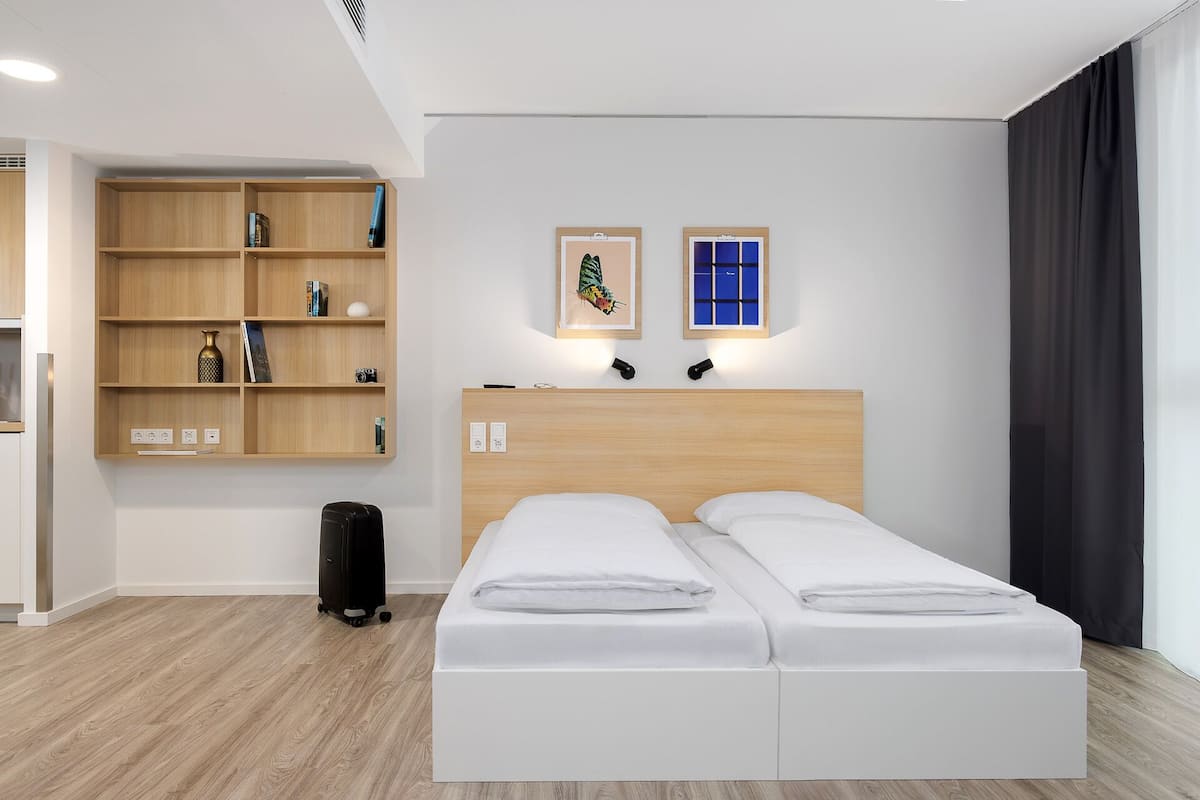 Une chambre d’hôtel moderne avec un lit double, une bibliothèque en bois et un petit bureau.