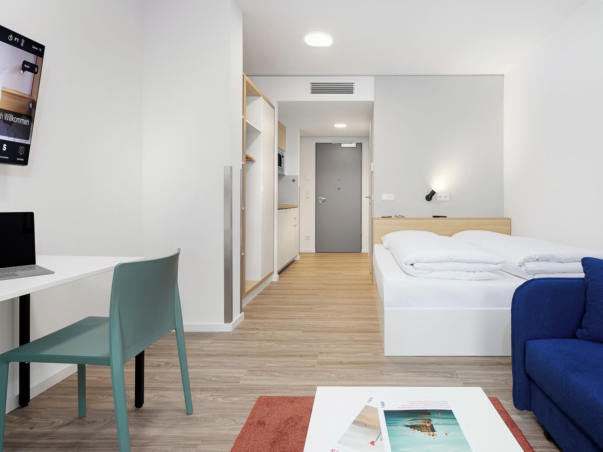 A hotel room with a desk, chair, bed, and a blue sofa.