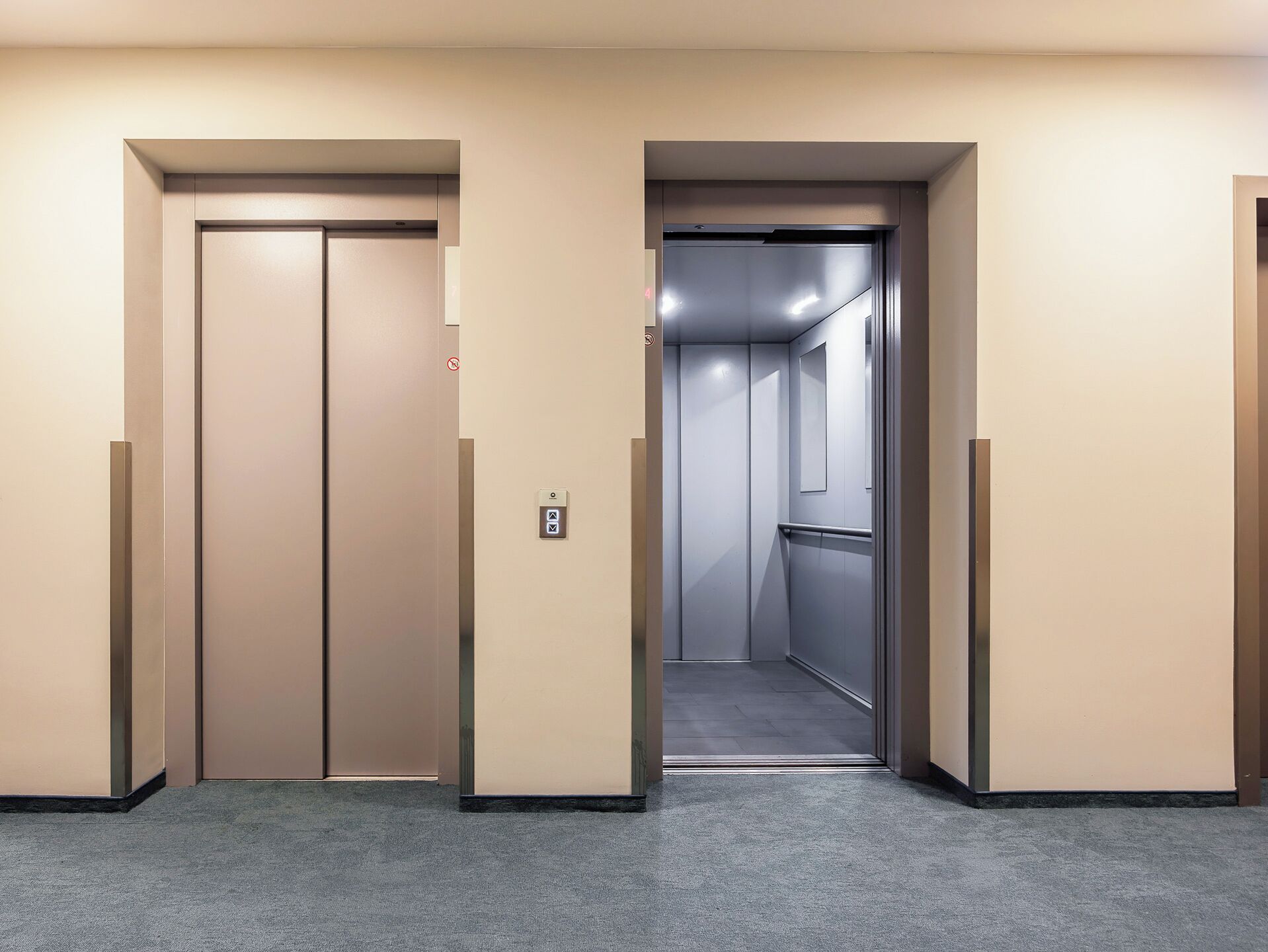 A hallway with two closed elevator doors, a carpeted floor, and a wall-mounted elevator control panel.