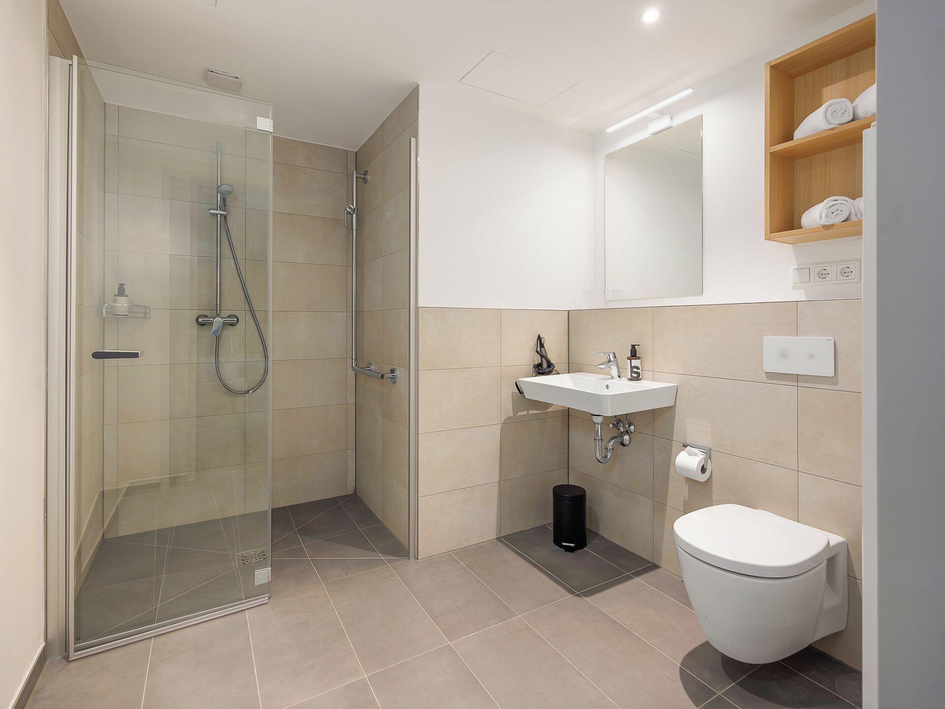 Een moderne badkamer met een douche met glazen wand, een witte wastafel en een toilet.