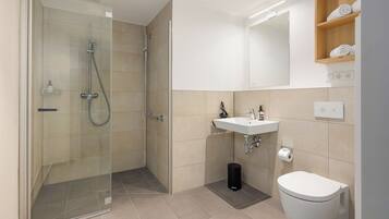 Een moderne badkamer met een douche met glazen wand, een witte wastafel en een toilet.