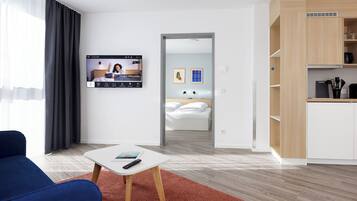 A modern hotel room with a bed, a TV, a desk, and a kitchenette.