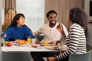 Una mesa de comedor con alimentos para el desayuno, como cruasanes, frutas y bebidas.