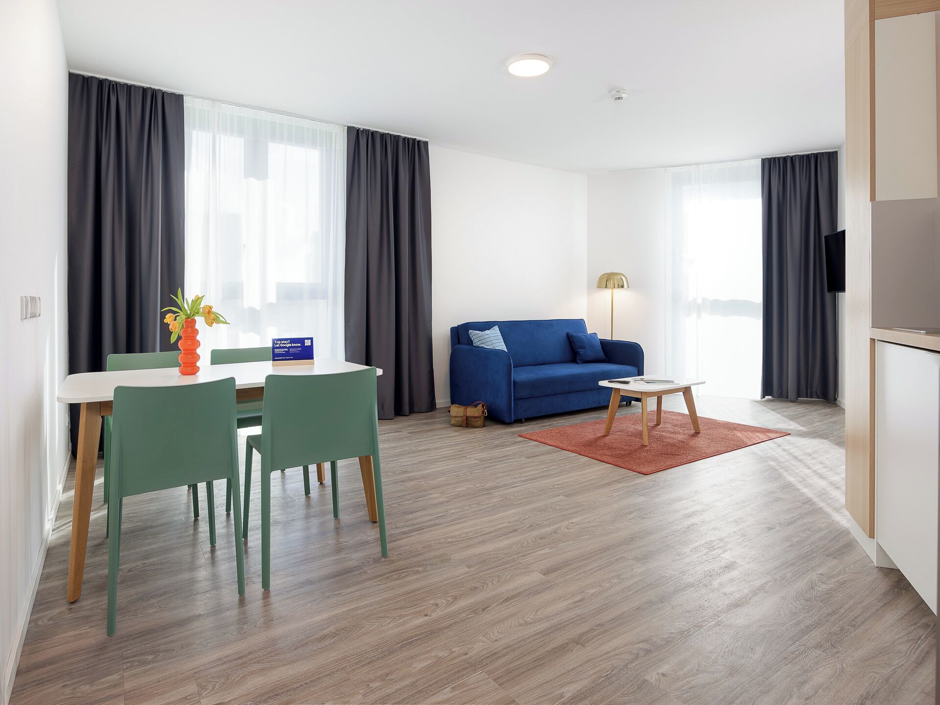 Ein modernes Wohnzimmer mit einem blauen Sofa, einem Esstisch mit Stühlen, einem kleinen Couchtisch und einer Lampe.