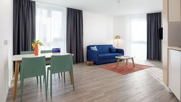 Ein modernes Wohnzimmer mit einem blauen Sofa, einem Esstisch mit Stühlen, einem kleinen Couchtisch und einer Lampe.