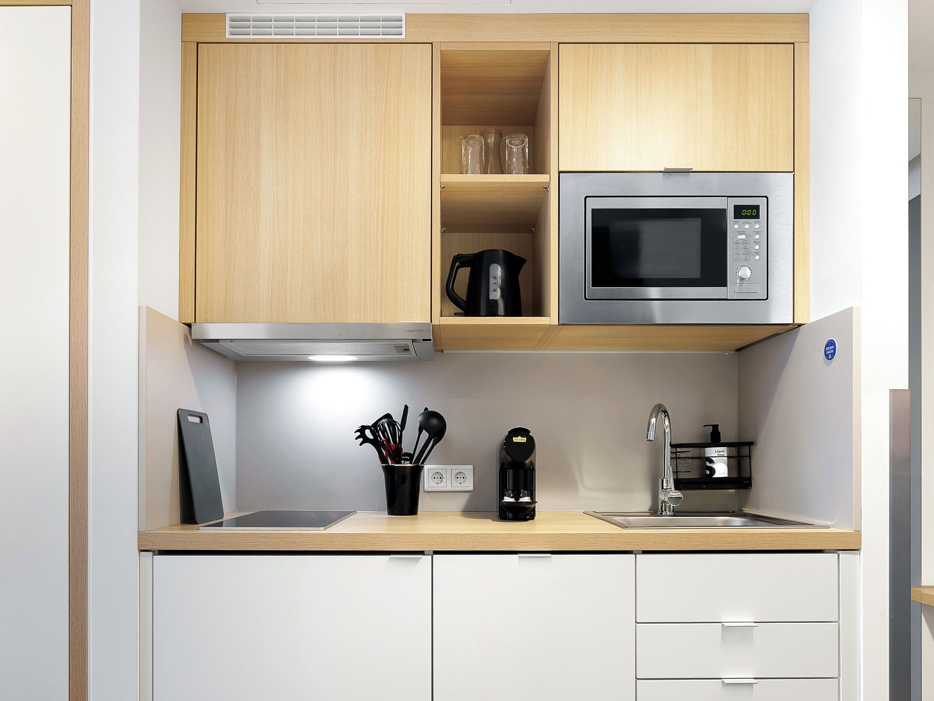 A modern kitchen with wooden cabinets, a stainless steel microwave, a coffee maker, and a sink.