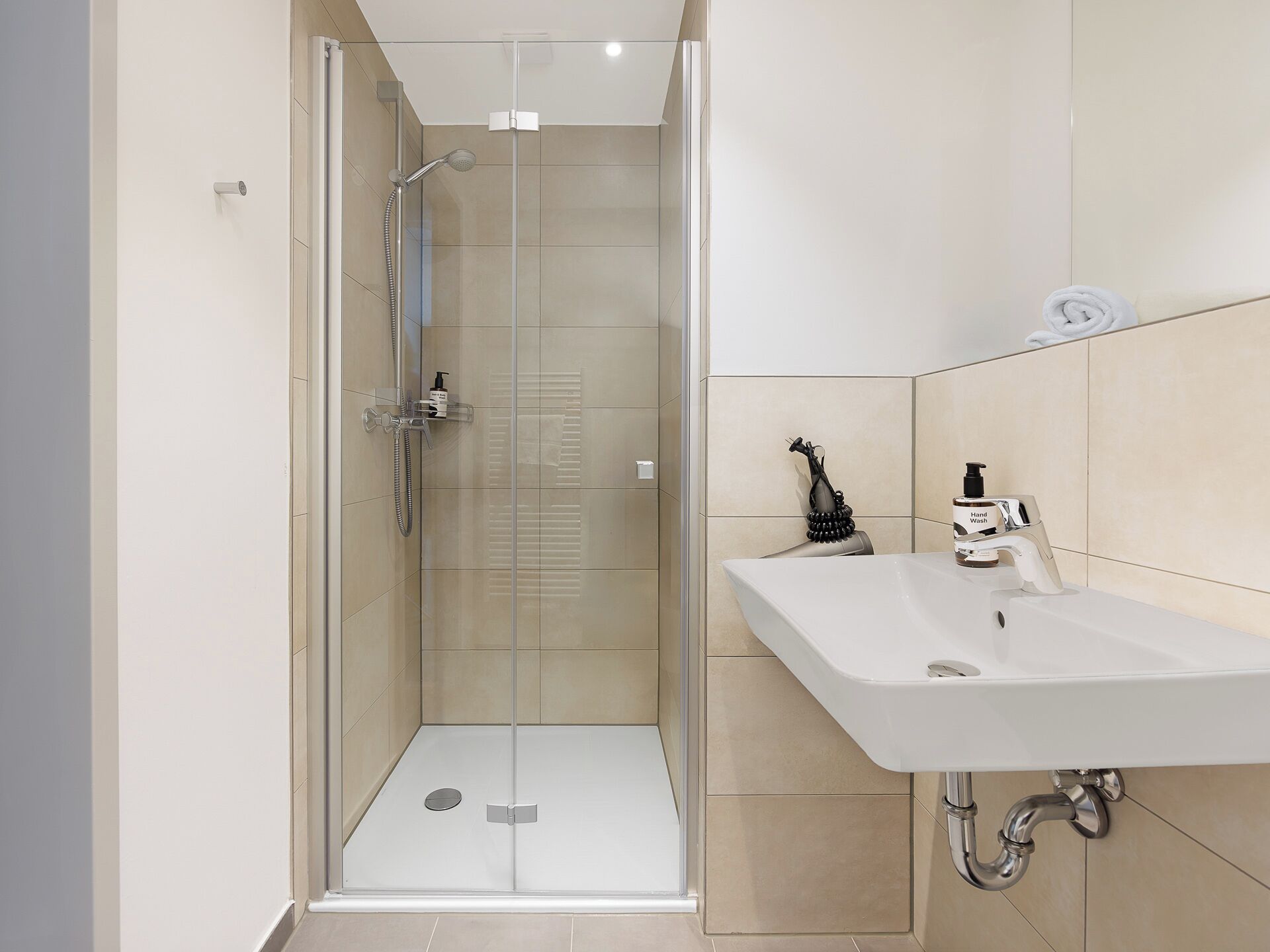 A modern bathroom with a glass-enclosed shower, a white sink, and beige tiles.