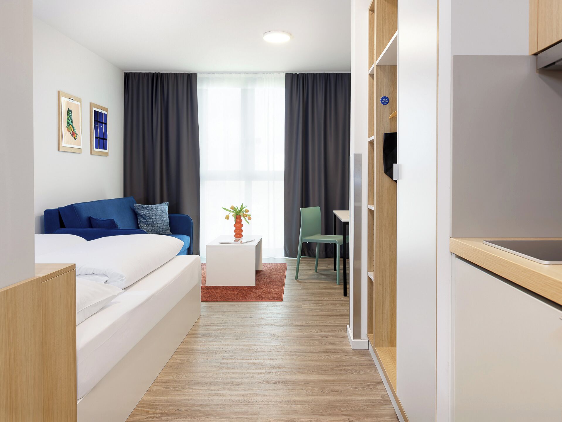Een moderne hotelkamer met een bed, een tafeltje met een vaas, een stoel, een bureau en een kitchenette.